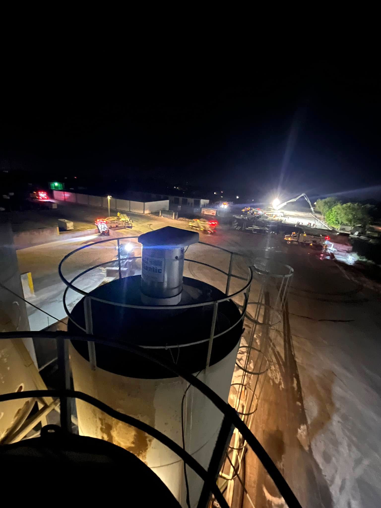 Night view from high on a railed tank, looking out over a floodlit jobsite