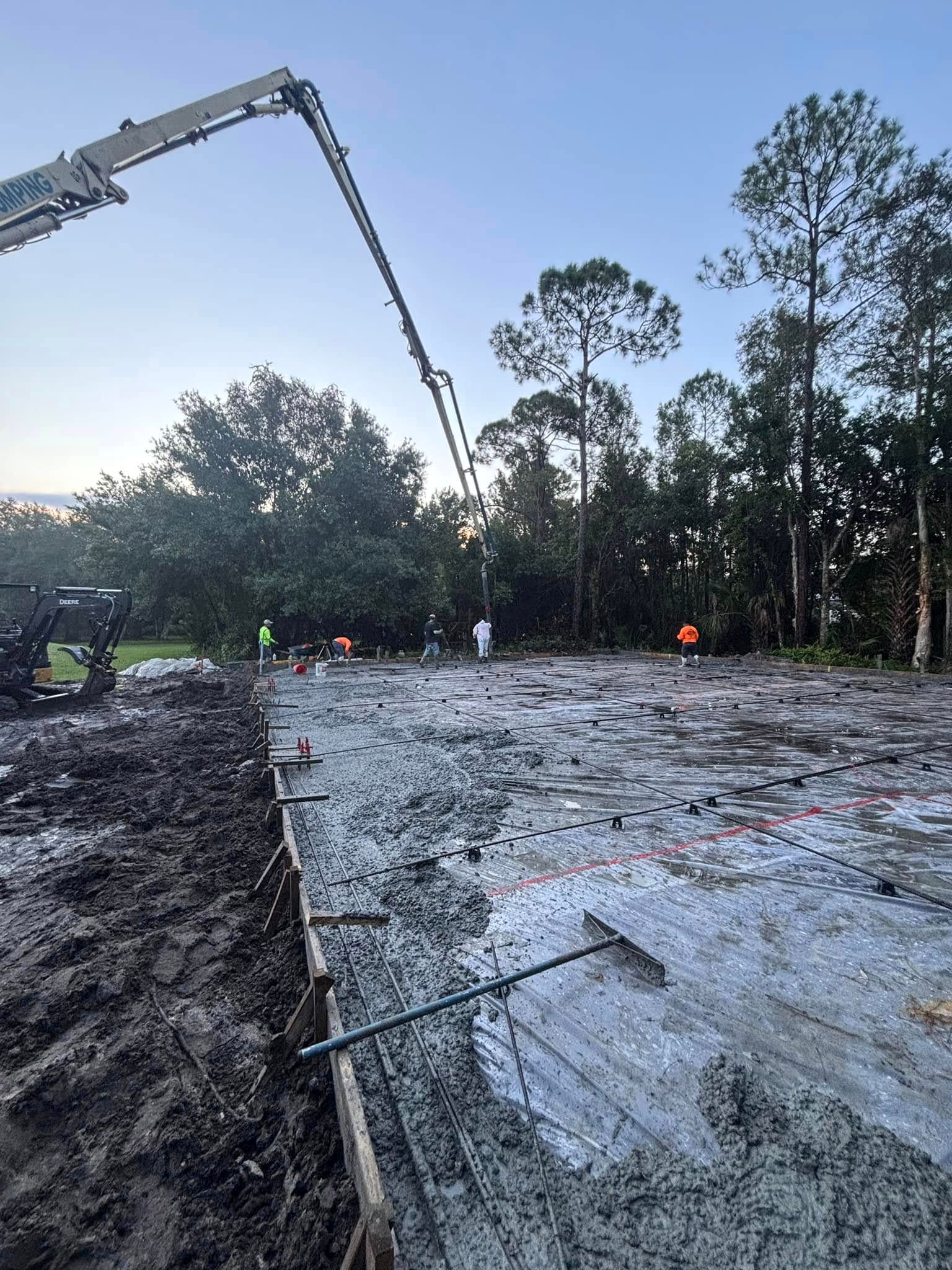 Large slab of fresh concrete inside wood forms, with a pump boom overhead and workers at the far edge